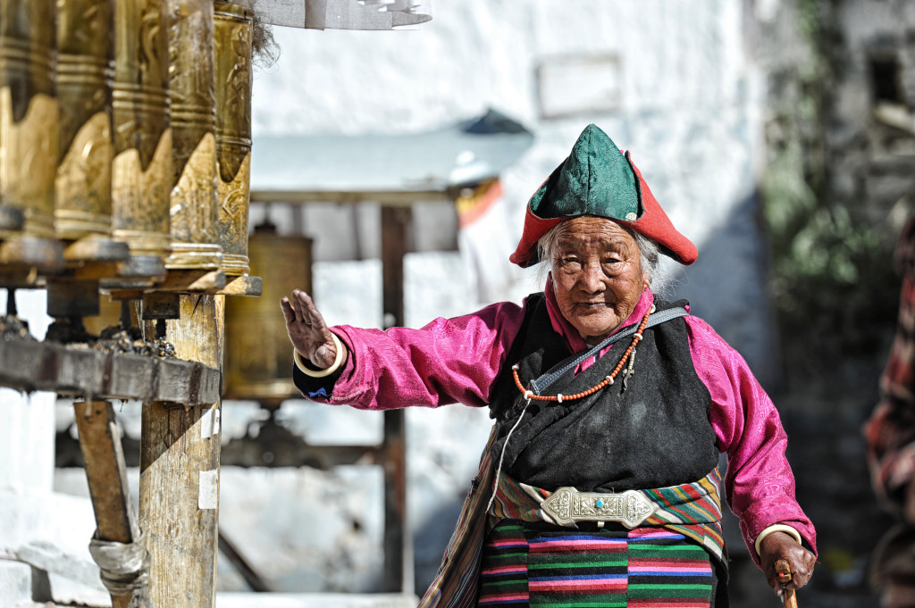 shutterstock_139379312 tibetan woman by religious prayer wheel buddhism